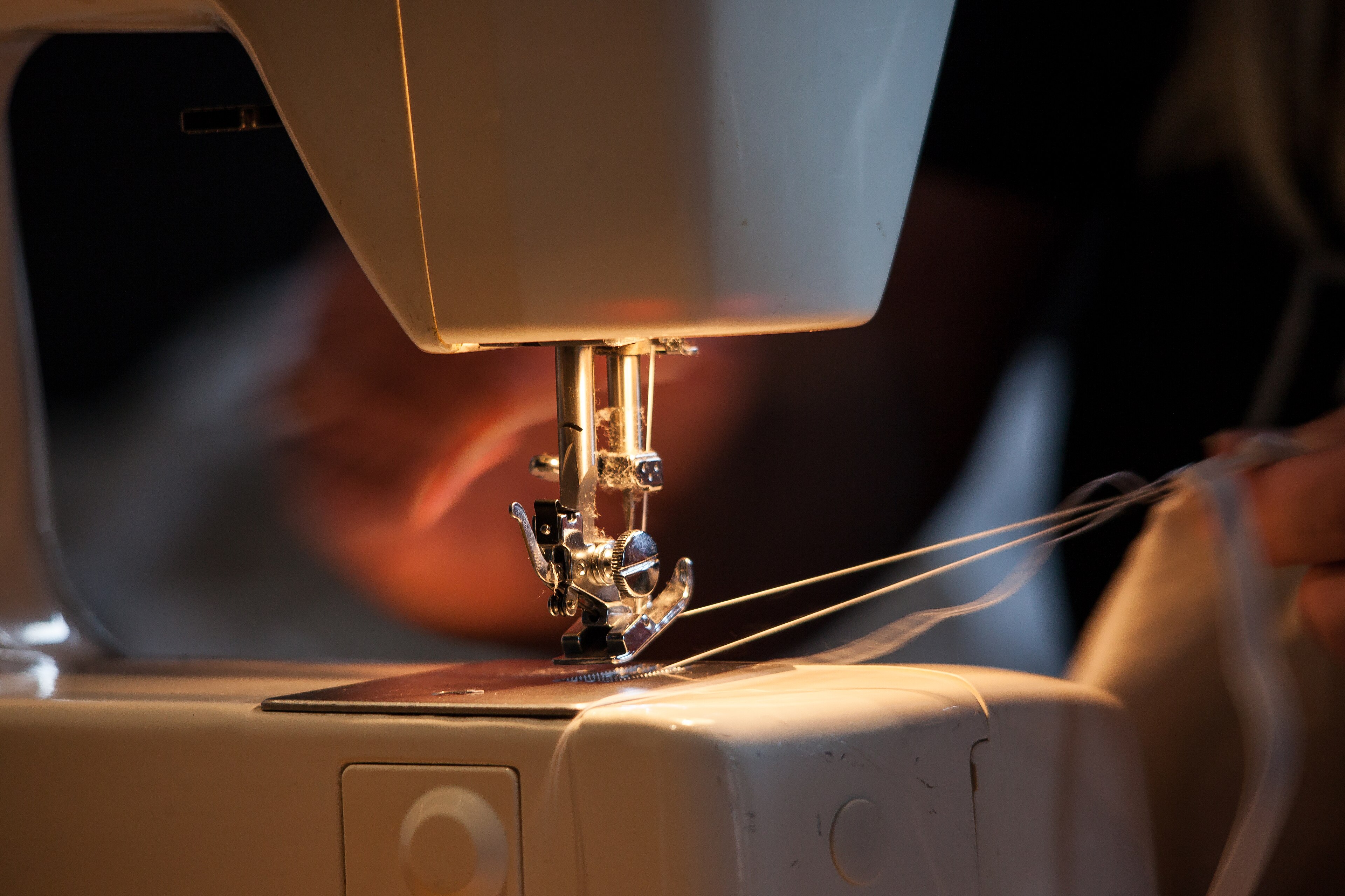 Handen geleiden stof onder de naaivoet van een naaimachine in de showroom